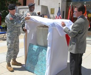 Two men uncover a time capsule in front of a set of flags