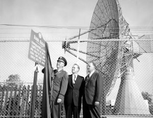 Military officer and officials in front of a Diana Radar sign